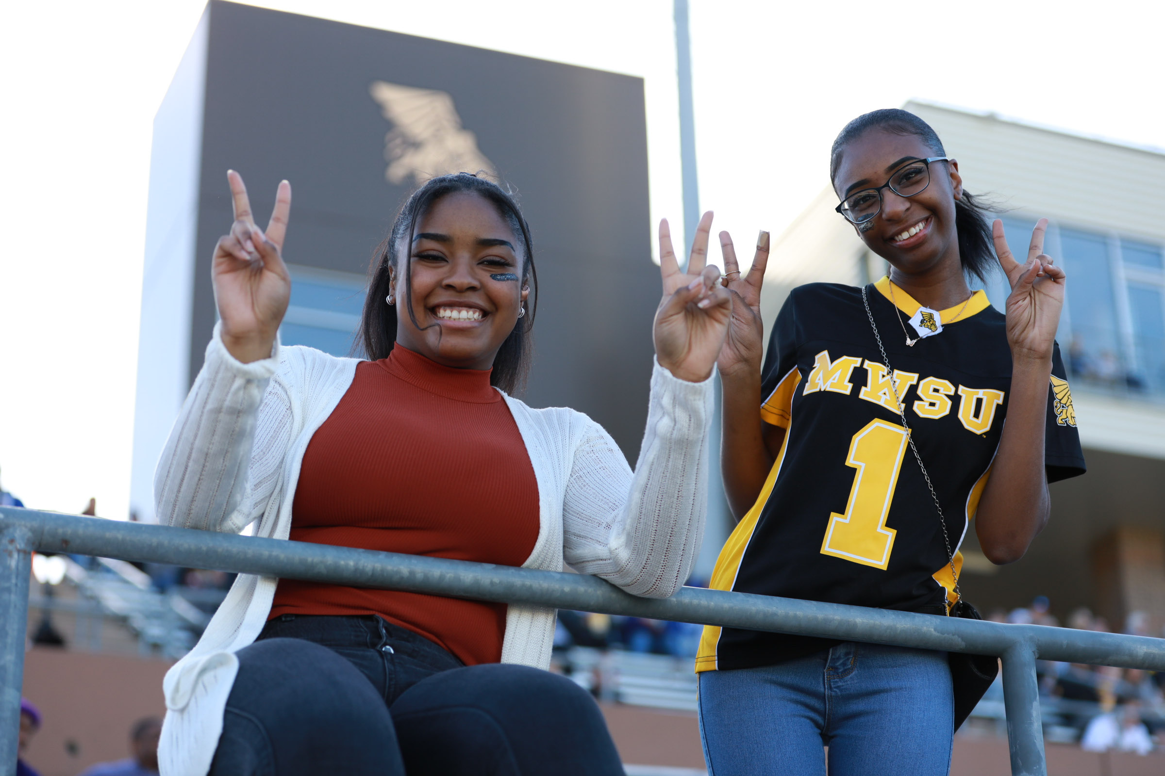 two students posing for the camera smiling and holding up peace signs