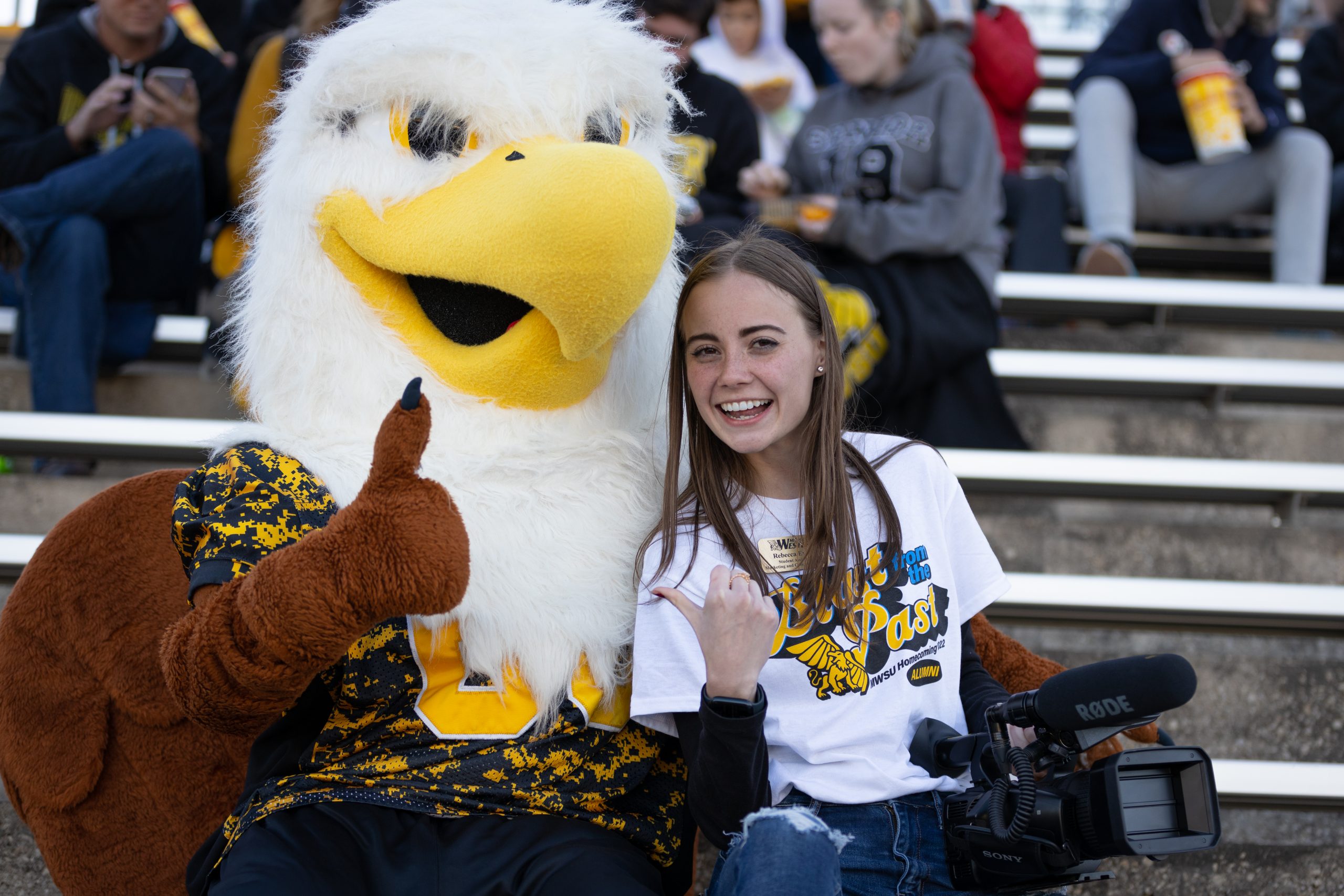 student holding a video camera posing with max the griffon both giving a thumbs up to the camera